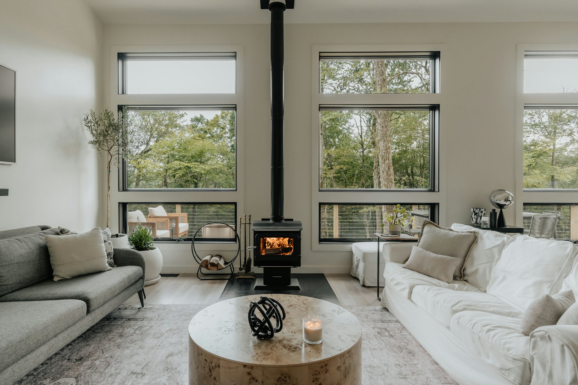 Bright living room with a wood stove between tall windows and light oak floors